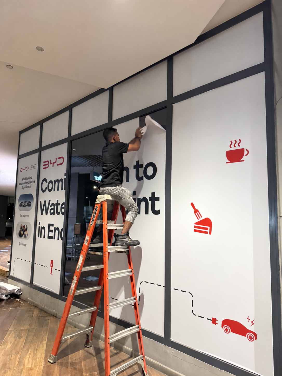Shopfront hoarding being installed on a ladder — Hoarding Sticker Printing by Garrison Productions, Singapore
